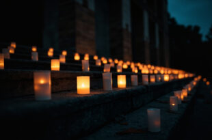 White memorial candles flickering on stone church steps at twilight creating pools of warm light