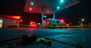 Crime scene tape and evidence markers around gas station at night with emergency vehicle lights