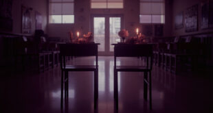 Empty school desks with memorial flowers and lit candles in soft window light