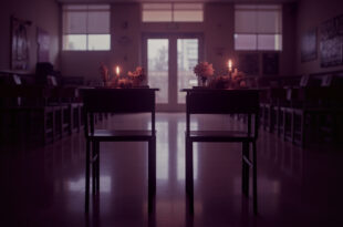 Empty school desks with memorial flowers and lit candles in soft window light