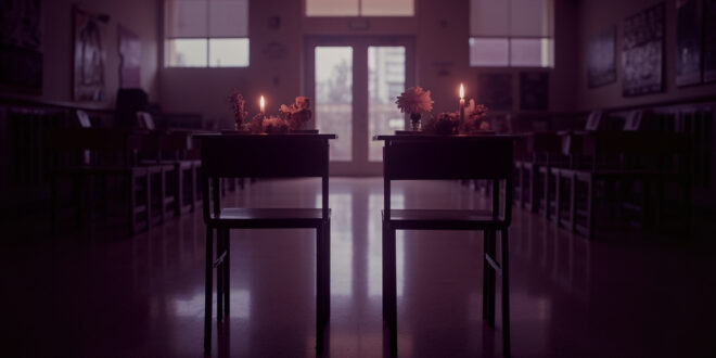 Empty school desks with memorial flowers and lit candles in soft window light