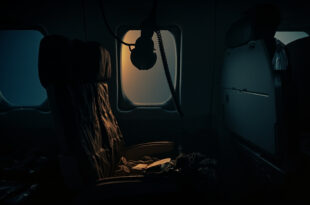 Empty airplane seat with deployed oxygen mask and scattered personal items in dimly lit aircraft cabin