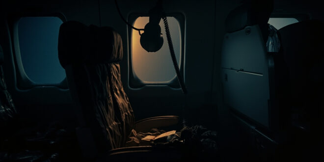 Empty airplane seat with deployed oxygen mask and scattered personal items in dimly lit aircraft cabin