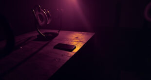 Dark smartphone on wooden desk surrounded by turned off ring lights and recording equipment in empty studio