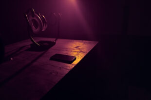 Dark smartphone on wooden desk surrounded by turned off ring lights and recording equipment in empty studio