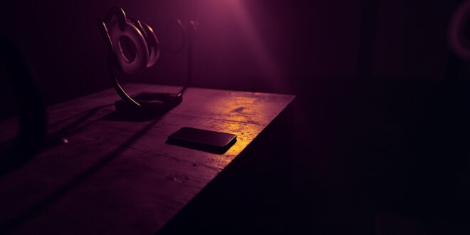 Dark smartphone on wooden desk surrounded by turned off ring lights and recording equipment in empty studio