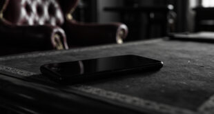 Black smartphone resting on ornate wooden desk in formal government office setting with rich burgundy and gold tones