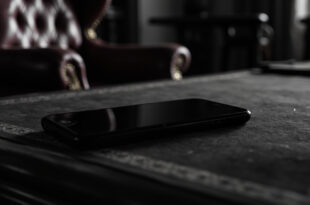 Black smartphone resting on ornate wooden desk in formal government office setting with rich burgundy and gold tones