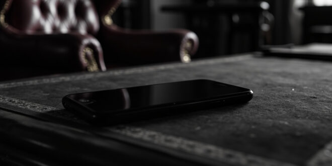 Black smartphone resting on ornate wooden desk in formal government office setting with rich burgundy and gold tones