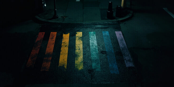 Black paint covers rainbow-striped crosswalk on empty city street at night