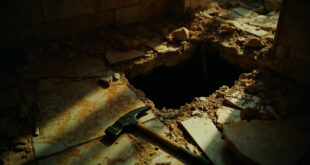 Torn bathroom tiles and scratched walls around small dark opening near damaged furniture