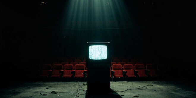 Empty theater stage with vintage television set under spotlight, red velvet seats in darkness