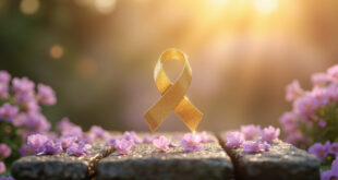 Golden cancer awareness ribbon floating above scattered flower petals on weathered stone surface in garden setting