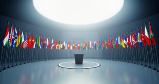 Twenty-six national flags arranged in semicircle around empty diplomatic conference podium in blue and gold minimalist setting