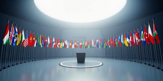 Twenty-six national flags arranged in semicircle around empty diplomatic conference podium in blue and gold minimalist setting