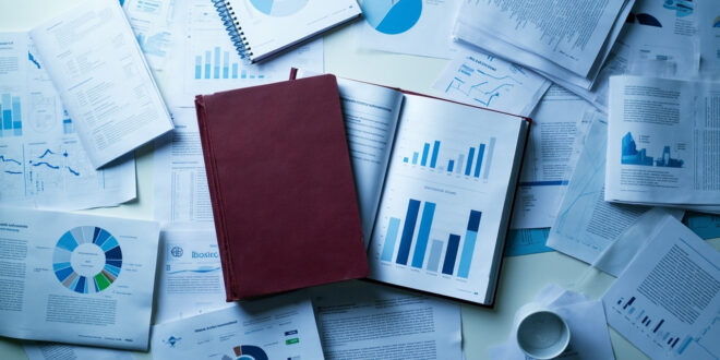 Bound research report surrounded by educational policy documents and statistical charts on institutional desk