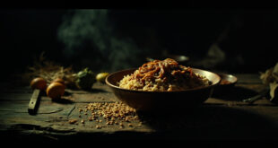 Bowl of lentils and rice dish surrounded by sparse cooking ingredients on weathered wooden surface