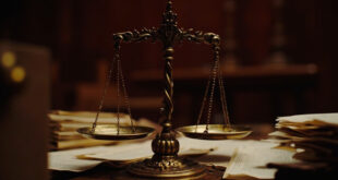 Brass scales of justice on wooden judicial bench with formal legal documents and case folders arranged around it