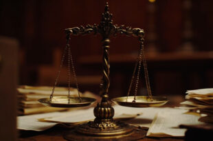 Brass scales of justice on wooden judicial bench with formal legal documents and case folders arranged around it