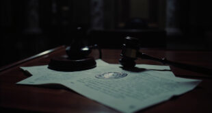 Official indictment papers and wooden gavel on dark wooden courthouse desk with dramatic lighting