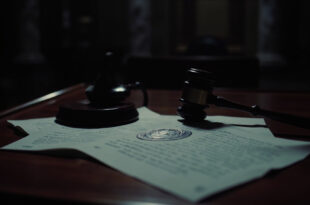 Official indictment papers and wooden gavel on dark wooden courthouse desk with dramatic lighting