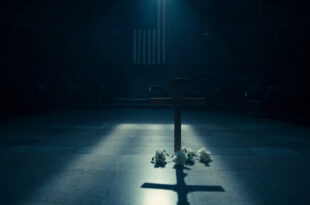 Wooden cross with white flowers on marble steps in empty political venue with American flag backdrop
