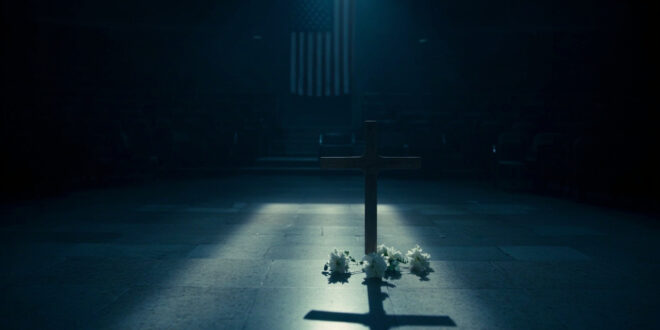 Wooden cross with white flowers on marble steps in empty political venue with American flag backdrop