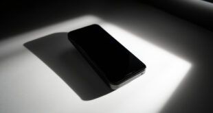 Black smartphone lying on white surface under dramatic studio lighting with geometric shadow patterns