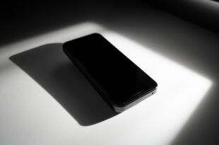 Black smartphone lying on white surface under dramatic studio lighting with geometric shadow patterns