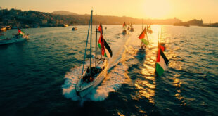 Fleet of vessels with Palestinian flags sailing from Mediterranean port at sunset