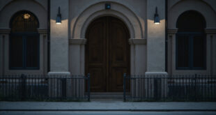 Empty synagogue entrance with wooden doors, security camera, and stone architecture on quiet street