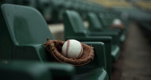 Baseball resting in brown leather glove on green stadium seat with empty rows stretching behind
