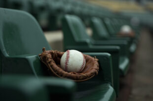 Baseball resting in brown leather glove on green stadium seat with empty rows stretching behind
