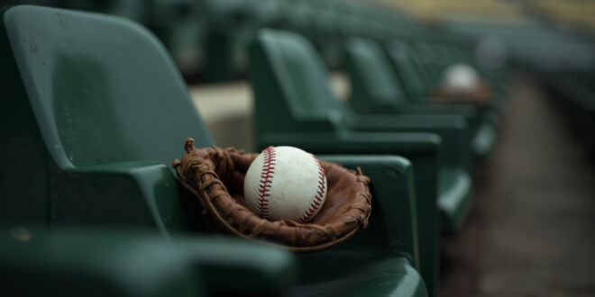 Baseball resting in brown leather glove on green stadium seat with empty rows stretching behind