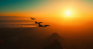 Military jets flying over desert mountains with government buildings visible below in orange evening light