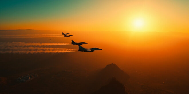 Military jets flying over desert mountains with government buildings visible below in orange evening light