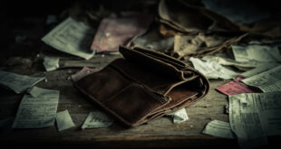 Empty wallet lies open beside unpaid bills and basic household items on a kitchen table