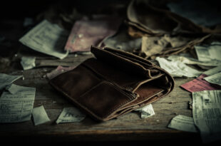 Empty wallet lies open beside unpaid bills and basic household items on a kitchen table