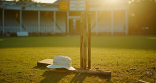 White umpire cap placed on cricket stumps in empty ground with traditional pavilion background