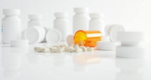 Orange prescription bottle spilled with white pills scattered across clean medical counter surface.