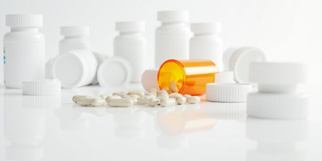 Orange prescription bottle spilled with white pills scattered across clean medical counter surface.