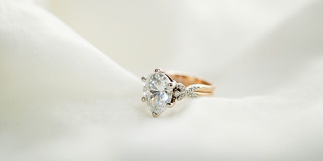 Close-up of sparkling diamond engagement ring on white silk fabric with soft lighting