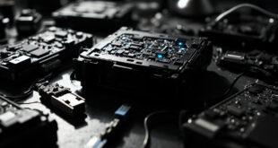 Black satellite receiver with opened casing showing circuit boards on metal table with technical documentation