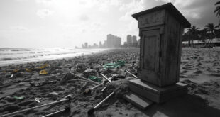 Empty wooden podium with microphone stands on Copacabana beach, scattered protest banners in sand, city buildings in background