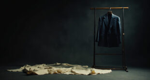 Navy blazer on stand in minimalist fashion studio with fabric samples and design sketches scattered on table.