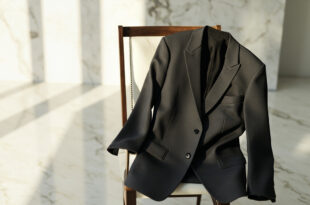 Charcoal gray blazer with soft tailoring draped over marble chair in bright atelier space