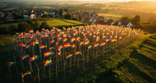 Rainbow flags fluttering on poles across rolling green hills of rural village setting