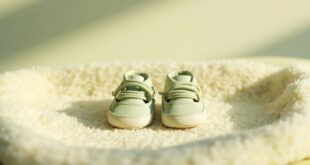 Two identical pairs of tiny baby shoes arranged on a soft cream blanket in warm lighting.