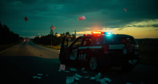 Police car with flashing blue lights parked on empty highway shoulder at twilight with warning ticket on asphalt