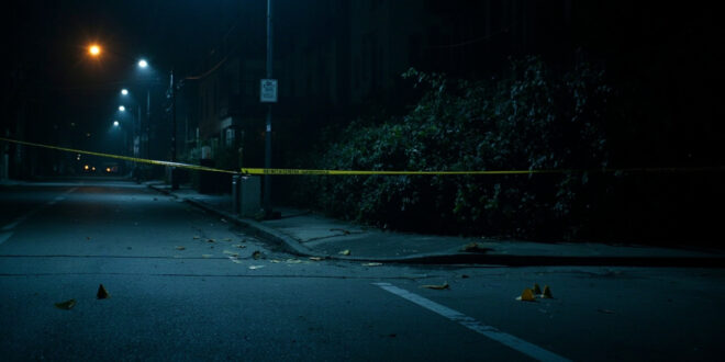 Police evidence markers and yellow tape cordoning off bushes along a dimly lit residential street